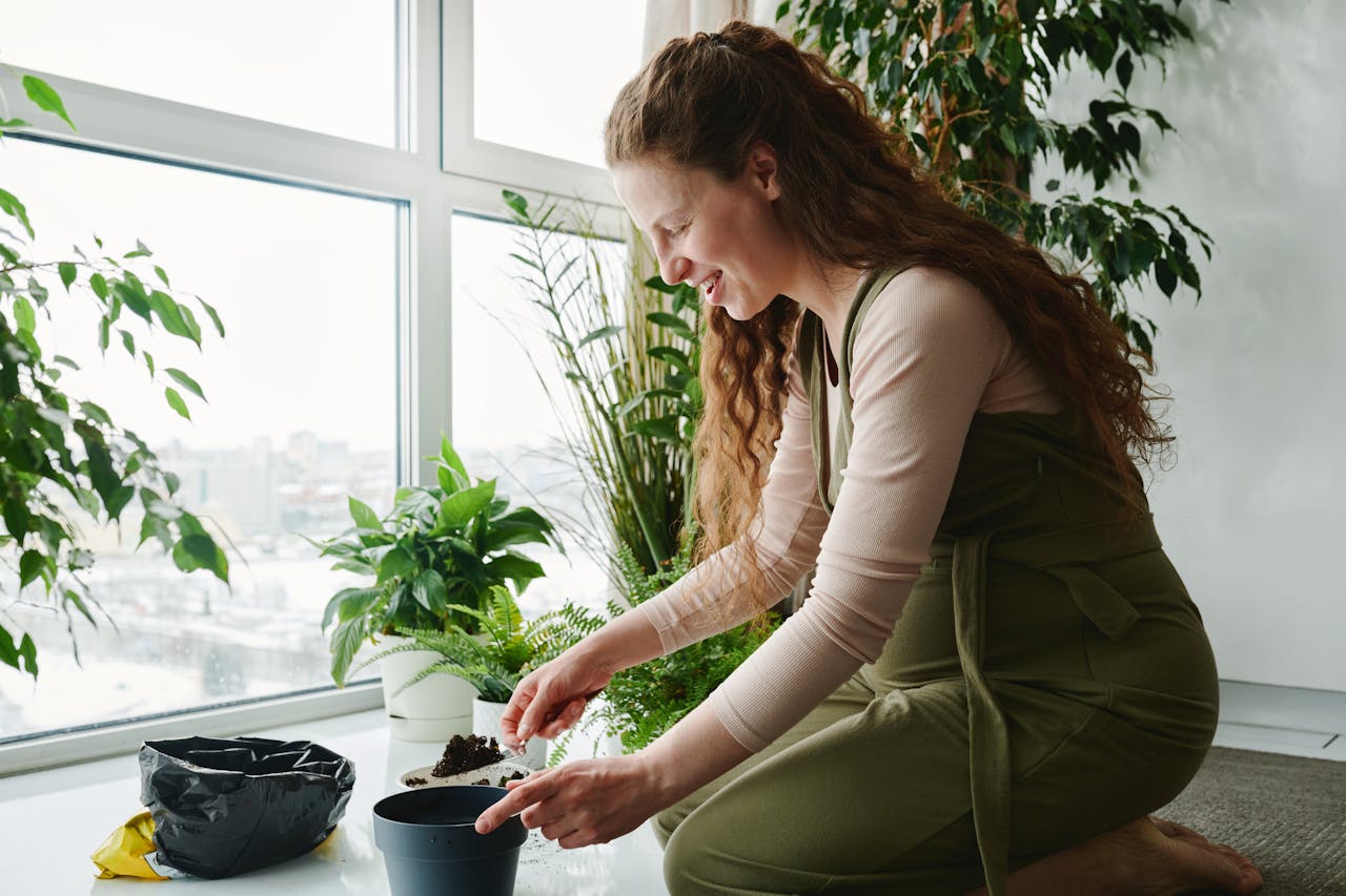 about-us-img Pregnant woman planting indoors with trowel, surrounded by green plants.
